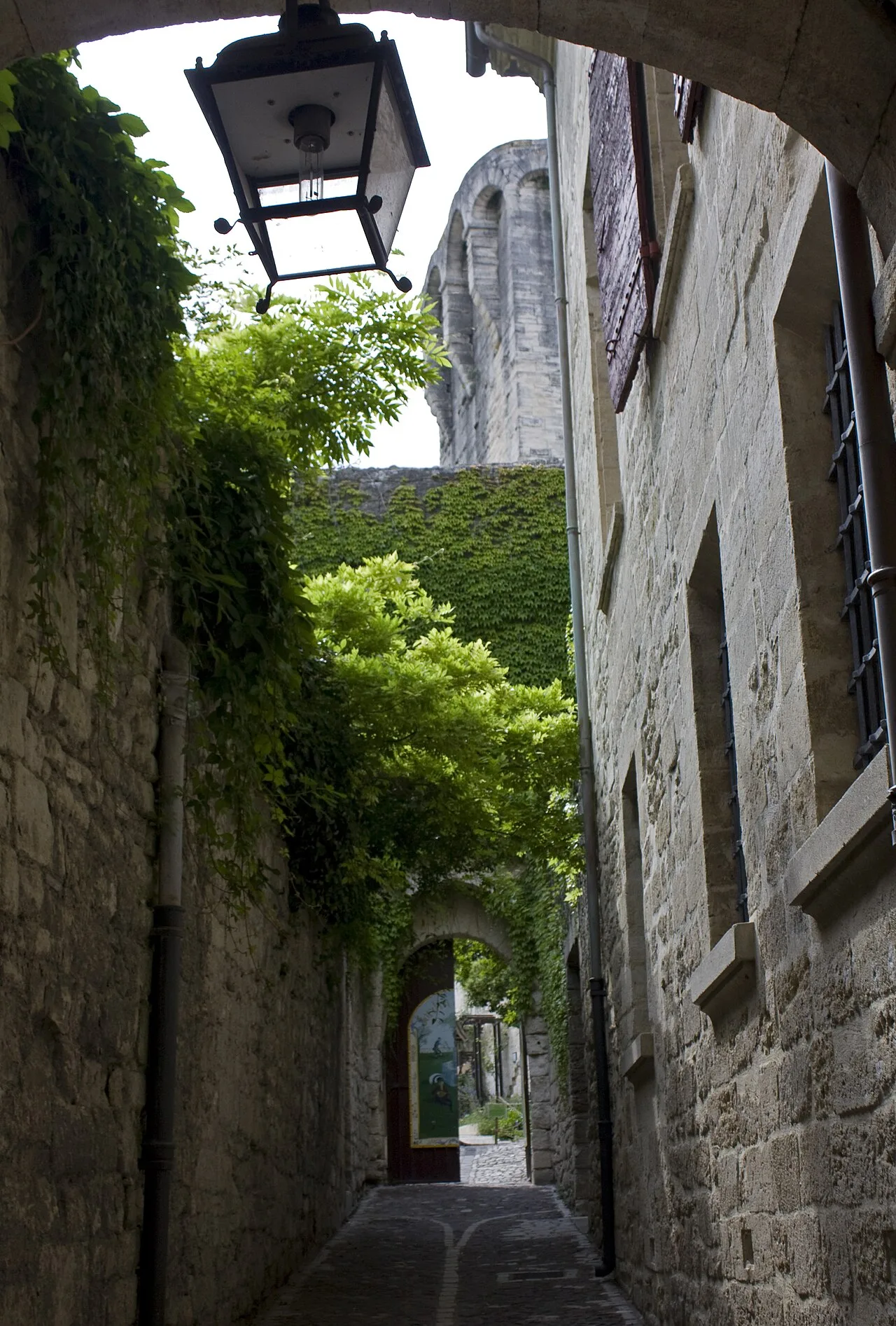 Passage pavé bordé de murs anciens et de végétation vers le jardin médiéval d’Uzès
